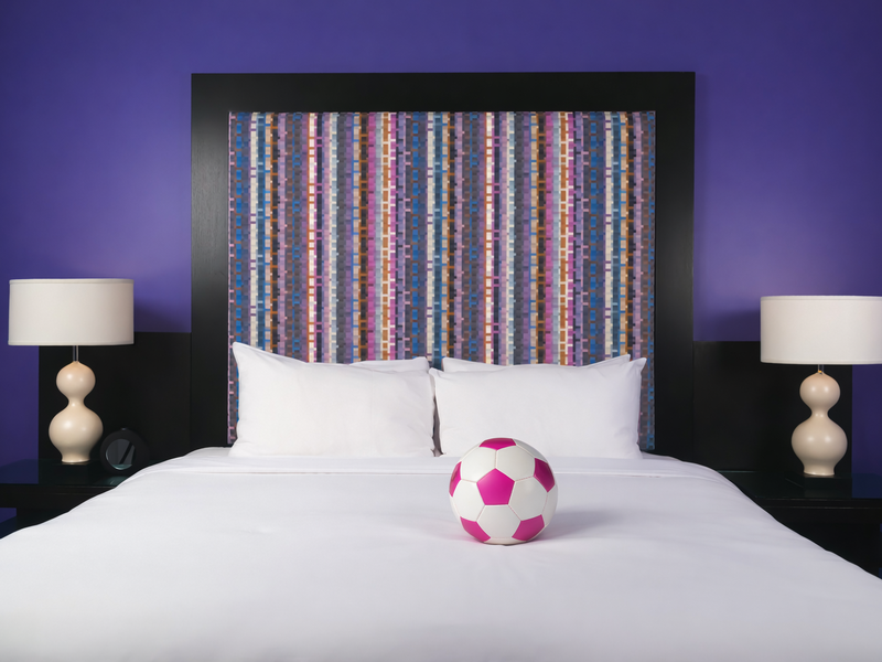 Pink soccer ball on a white bed with a colourful striped headboard in a room at OPUS Vancouver